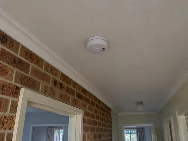 Ceiling smoke alarm in a hallway with brick wall and white trim in Brookvale